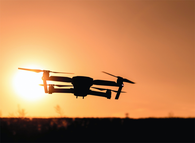 Image d'un drone qui vol face au soleil couchant.